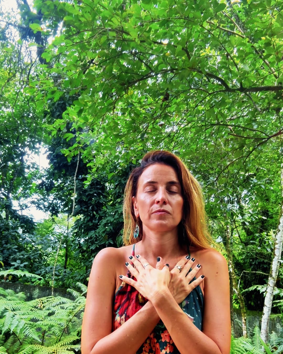 Danielle in a garden, eyes closed, arms crossed over her chest, hands resting on her shoulders